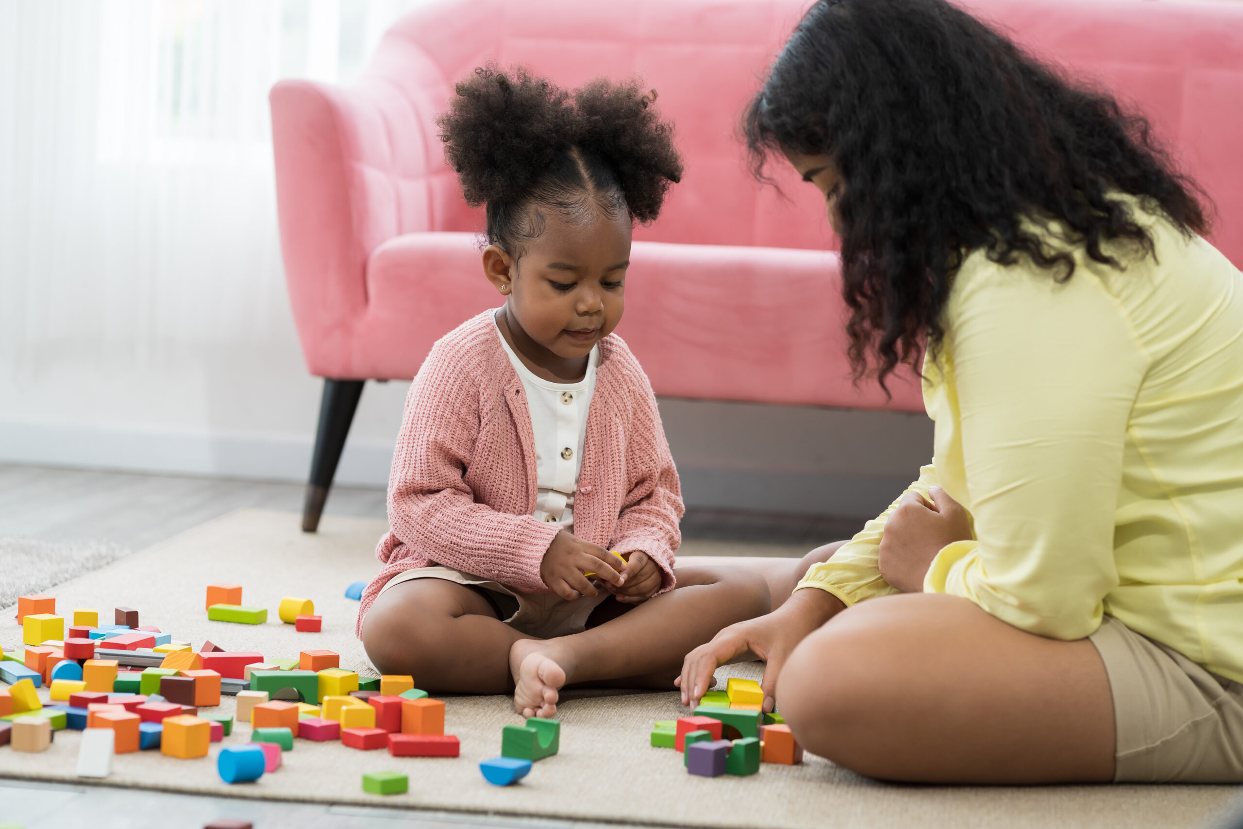Mother and daughter playing with toy at home. Happy African American girl kid playing with mom